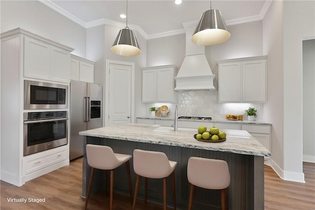 kitchen featuring appliances with stainless steel finishes, backsplash, a center island with sink, decorative light fixtures, and white cabinets