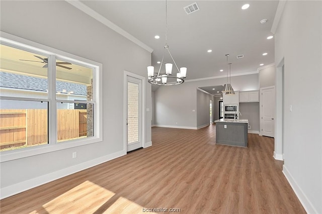 kitchen with ceiling fan with notable chandelier, hanging light fixtures, hardwood / wood-style flooring, ornamental molding, and an island with sink