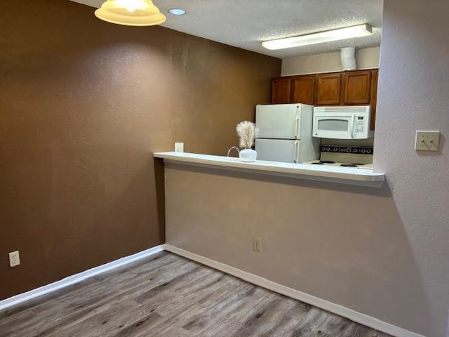 kitchen with white appliances, light hardwood / wood-style flooring, and a textured ceiling