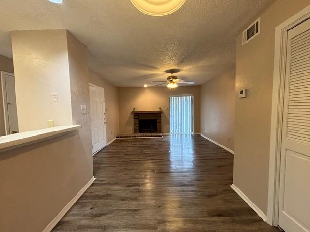 unfurnished living room with a brick fireplace, a textured ceiling, dark wood-type flooring, and ceiling fan