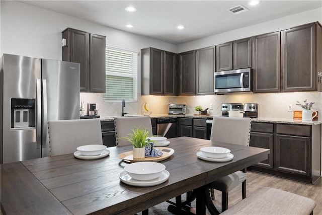 5745 Cerrillos Dr, Bryan, TX 77807 - kitchen featuring appliances with stainless steel finishes, dark brown cabinets, light wood finished floors, backsplash, and recessed lighting