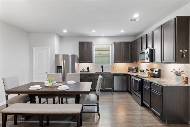 5745 Cerrillos Dr, Bryan, TX 77807 - kitchen featuring stainless steel appliances, a sink, dark brown cabinets, decorative backsplash, and light wood-style floors