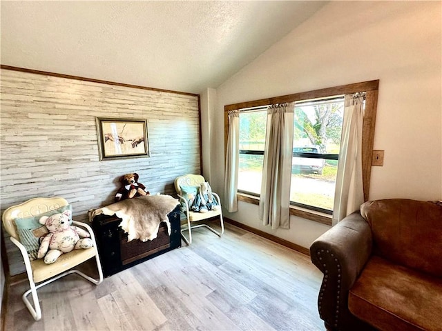 sitting room with baseboards, vaulted ceiling, light wood finished floors, and a textured ceiling