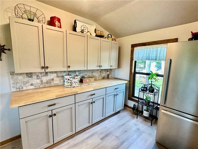 kitchen with light wood-style floors, freestanding refrigerator, backsplash, and vaulted ceiling
