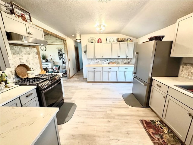 kitchen featuring light wood-style flooring, decorative backsplash, lofted ceiling, under cabinet range hood, and gas range oven
