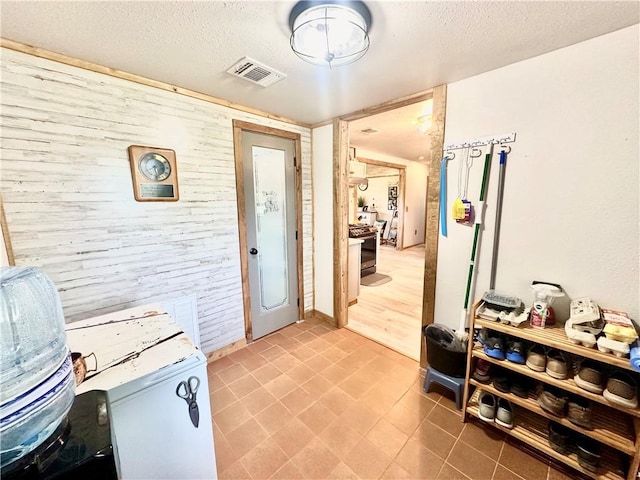 interior space with wooden walls, light tile patterned flooring, a textured ceiling, and visible vents
