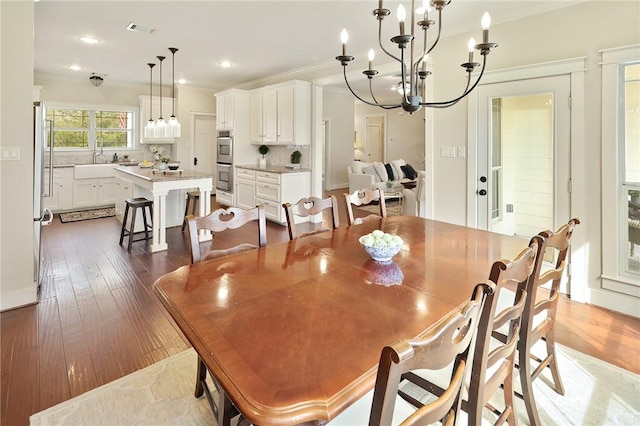 dining space with dark wood-type flooring, ornamental molding, sink, and an inviting chandelier