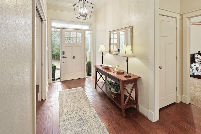 entrance foyer with dark hardwood / wood-style flooring, crown molding, and an inviting chandelier