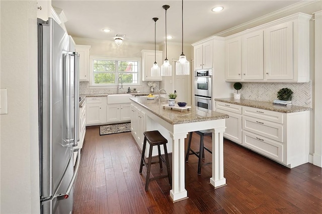 kitchen featuring a kitchen breakfast bar, appliances with stainless steel finishes, white cabinets, and a center island with sink