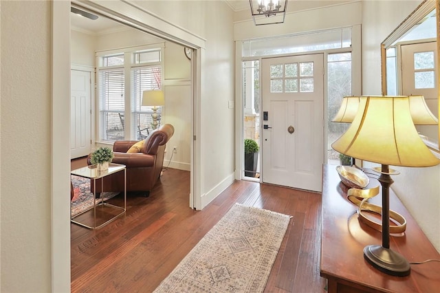 foyer entrance with ornamental molding, dark wood-type flooring, a wealth of natural light, and a chandelier