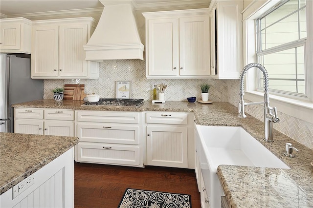 kitchen with premium range hood, appliances with stainless steel finishes, light stone countertops, and sink