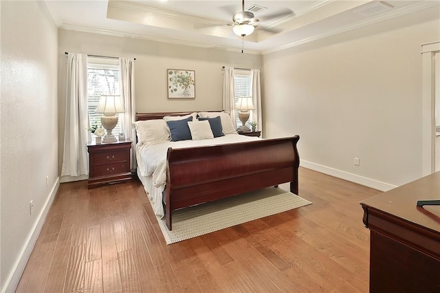 bedroom with hardwood / wood-style flooring, ceiling fan, ornamental molding, and a tray ceiling