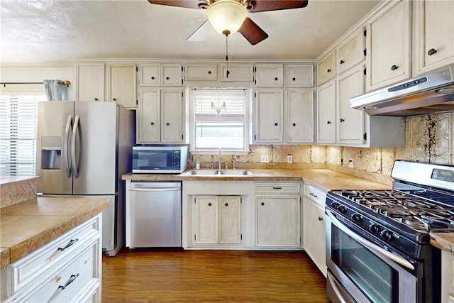 kitchen with dark wood-style flooring, ceiling fan, under cabinet range hood, a sink, and stainless steel appliances