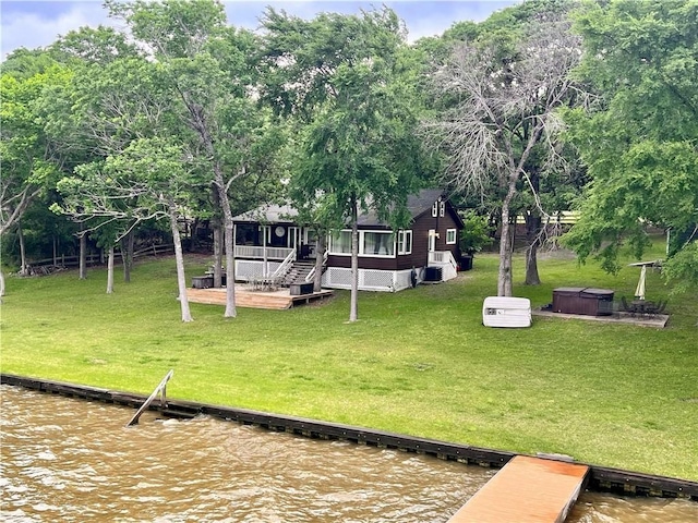 view of yard featuring a sunroom, a deck with water view, and a hot tub