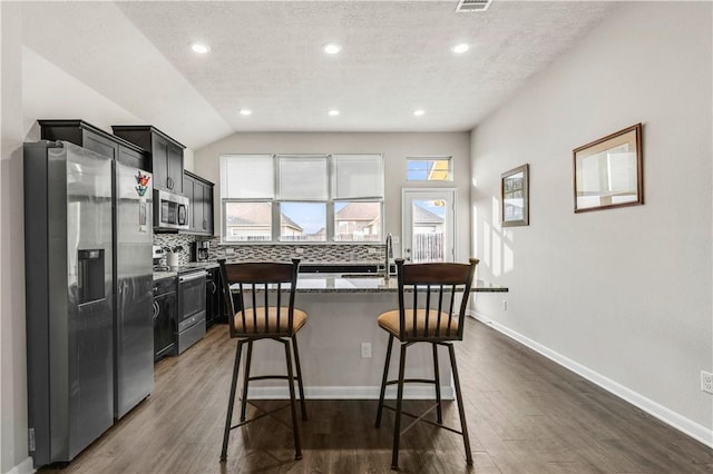 kitchen with stainless steel appliances, dark hardwood / wood-style floors, lofted ceiling, decorative backsplash, and a breakfast bar