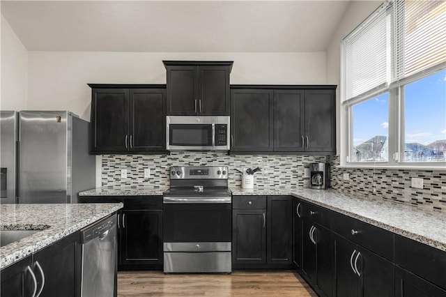 kitchen featuring stainless steel appliances, light hardwood / wood-style flooring, tasteful backsplash, and light stone counters