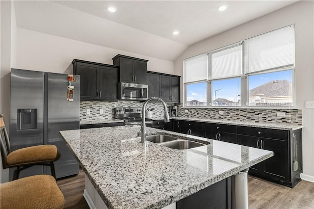 kitchen featuring lofted ceiling, backsplash, sink, an island with sink, and appliances with stainless steel finishes