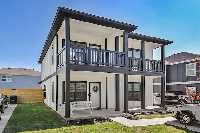 view of front facade with fence, covered porch, a balcony, and a front yard