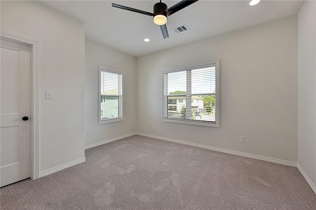 spare room with ceiling fan, light carpet, visible vents, and baseboards