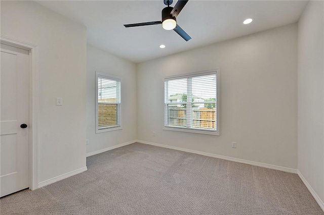 spare room with light colored carpet, baseboards, and a ceiling fan