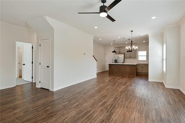 unfurnished living room with ornamental molding, baseboards, dark wood-style flooring, and ceiling fan with notable chandelier