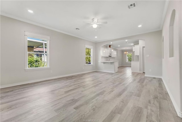 unfurnished living room with light wood finished floors, arched walkways, a ceiling fan, baseboards, and visible vents