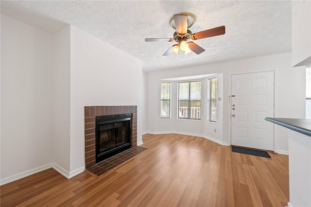 4441 Old College Rd, Bryan, TX 77801 - unfurnished living room featuring light wood-type flooring, a fireplace, a textured ceiling, and ceiling fan