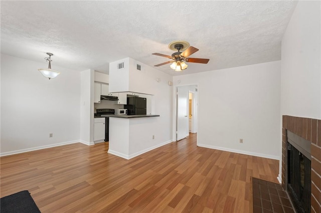 4441 Old College Rd, Bryan, TX 77801 - unfurnished living room featuring a tile fireplace, light wood finished floors, a textured ceiling, and ceiling fan