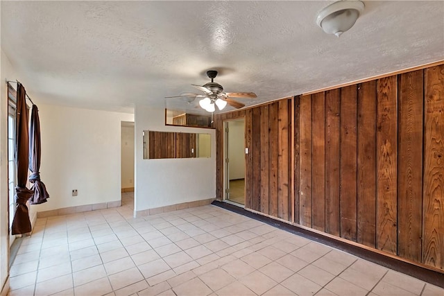 tiled empty room with ceiling fan, wood walls, and a textured ceiling