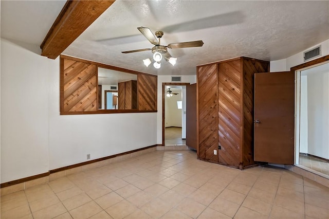 spare room featuring a textured ceiling, wooden walls, beamed ceiling, and ceiling fan