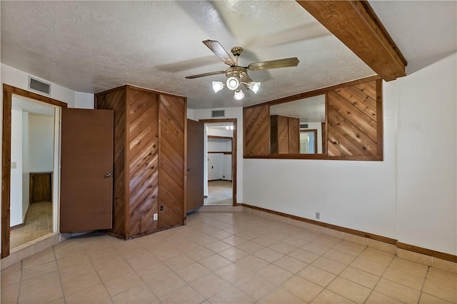 spare room with ceiling fan, a textured ceiling, and wood walls