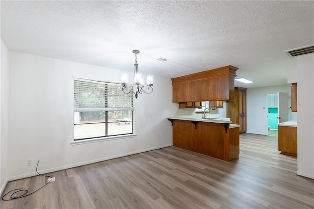 kitchen featuring sink, hanging light fixtures, light wood-type flooring, a kitchen breakfast bar, and kitchen peninsula