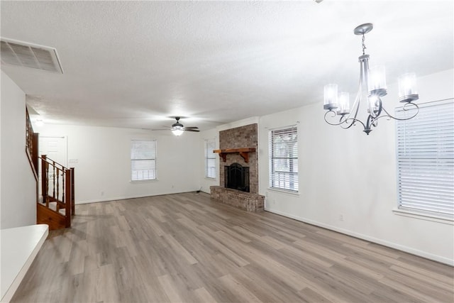 unfurnished living room featuring ceiling fan with notable chandelier, a fireplace, a textured ceiling, and light wood-type flooring