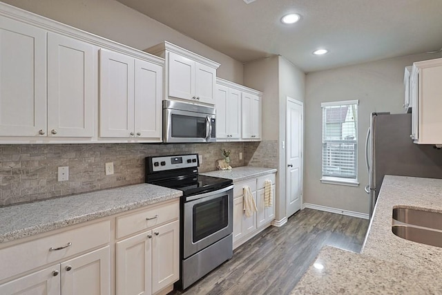 kitchen featuring white cabinetry, appliances with stainless steel finishes, hardwood / wood-style flooring, light stone countertops, and backsplash