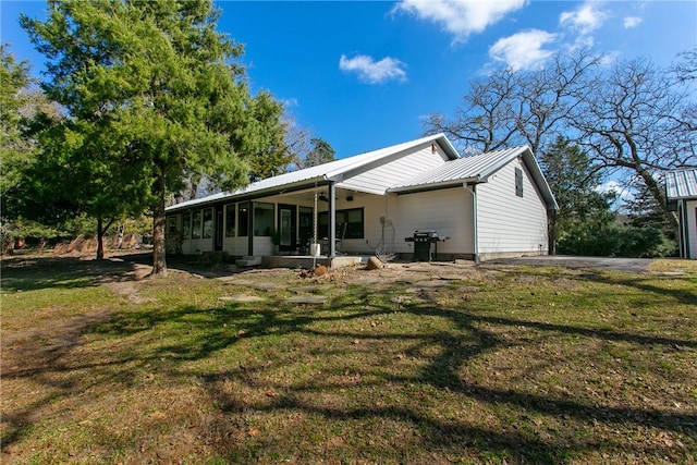 rear view of property with a sunroom, metal roof, and a yard