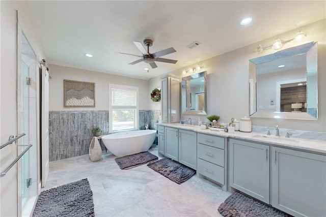 full bath featuring a freestanding tub, visible vents, a sink, and wainscoting