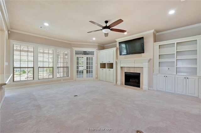 unfurnished living room featuring a tile fireplace, light carpet, crown molding, and ceiling fan