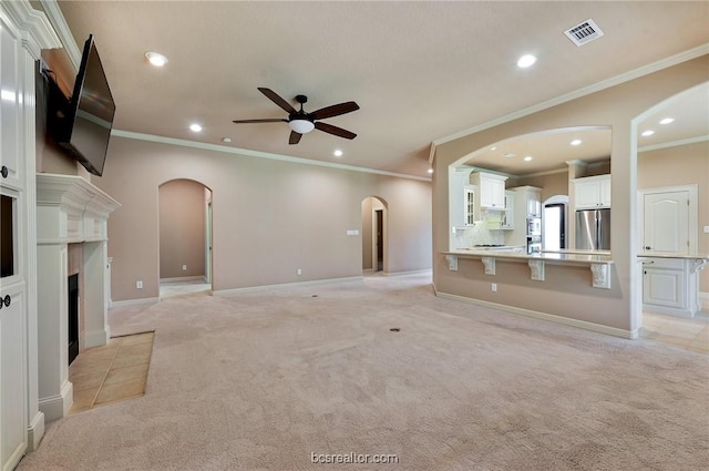 unfurnished living room featuring light colored carpet, ceiling fan, and ornamental molding