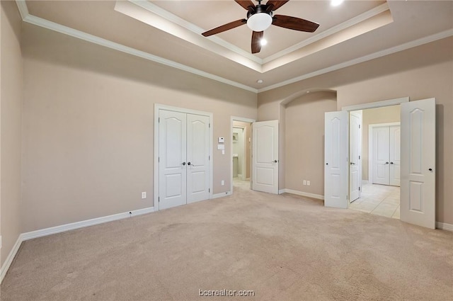 unfurnished bedroom with a raised ceiling, ceiling fan, light colored carpet, and ornamental molding