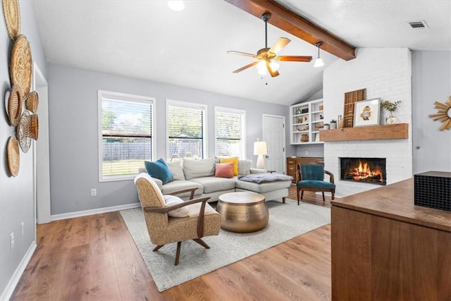 living room featuring light wood-type flooring, lofted ceiling with beams, a brick fireplace, and ceiling fan