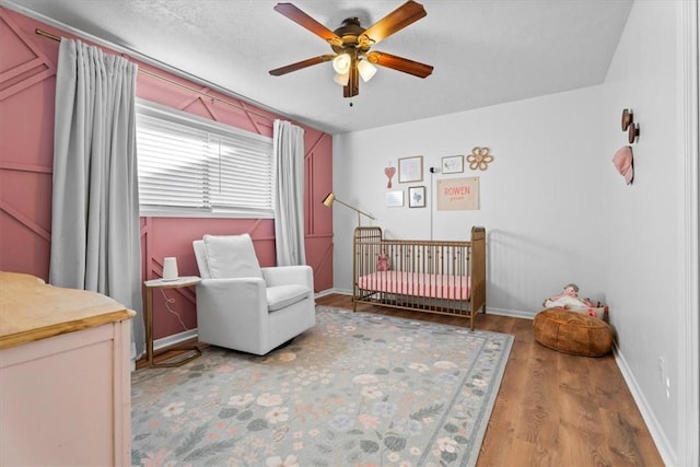 bedroom with ceiling fan, wood-type flooring, and a crib