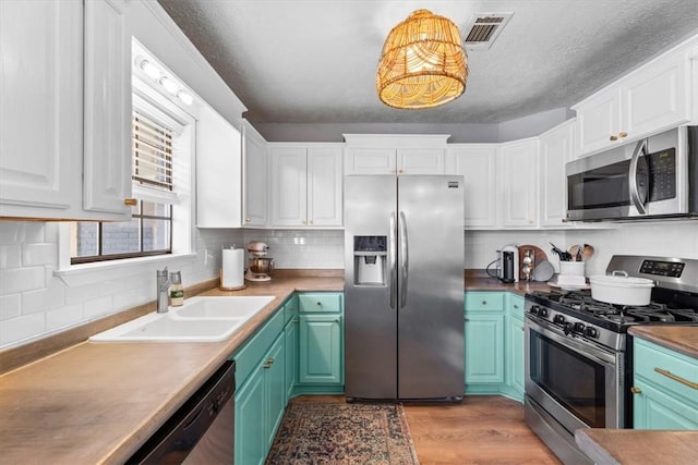 kitchen with appliances with stainless steel finishes, a textured ceiling, sink, wood-type flooring, and white cabinetry