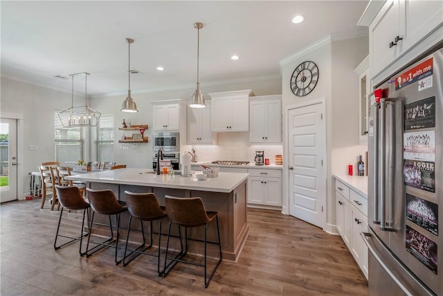 kitchen featuring pendant lighting, a breakfast bar, an island with sink, appliances with stainless steel finishes, and white cabinetry