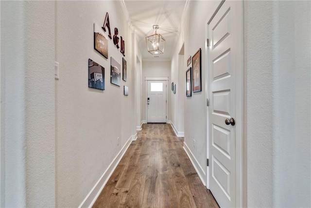 hallway with a chandelier, wood-type flooring, and crown molding