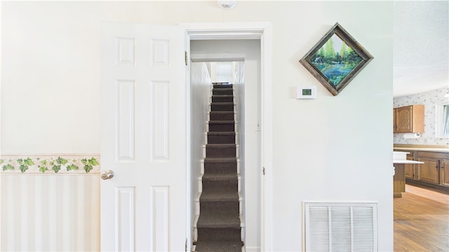 stairway with wallpapered walls, visible vents, and wood finished floors