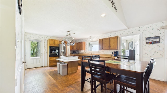 dining area with wallpapered walls, a notable chandelier, a healthy amount of sunlight, and light wood-style flooring