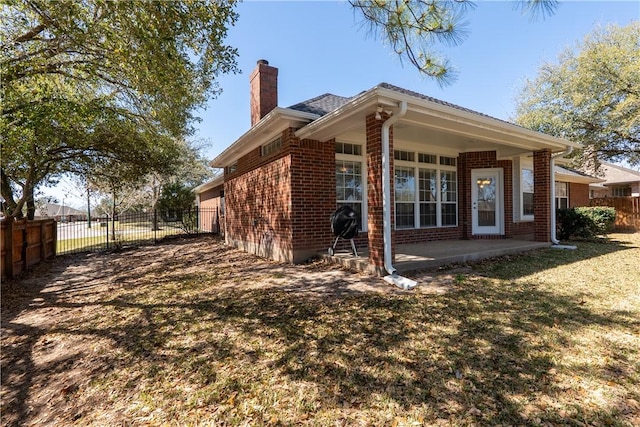 rear view of property featuring a patio area, fence, brick siding, and a chimney