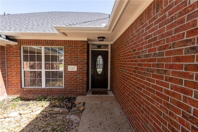 doorway to property featuring brick siding and a shingled roof