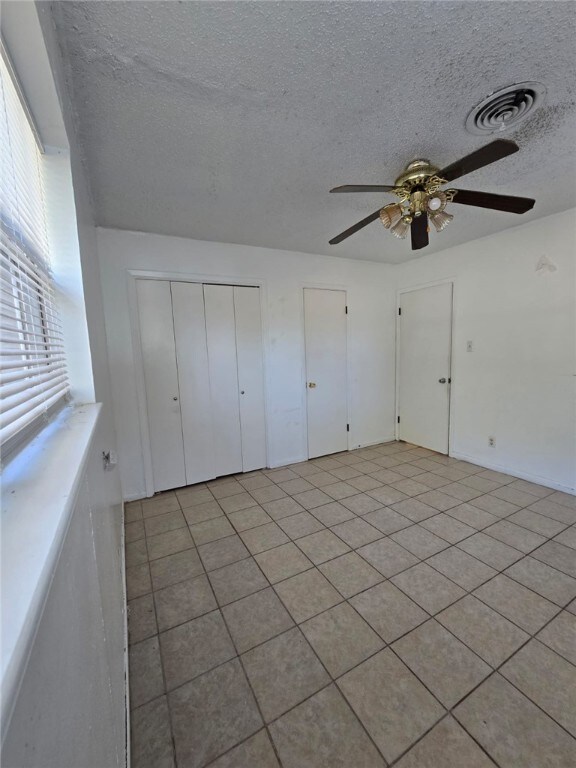 unfurnished bedroom with ceiling fan, light tile patterned floors, and a textured ceiling