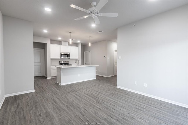 kitchen with stainless steel appliances, white cabinetry, hanging light fixtures, dark hardwood / wood-style flooring, and a kitchen island with sink